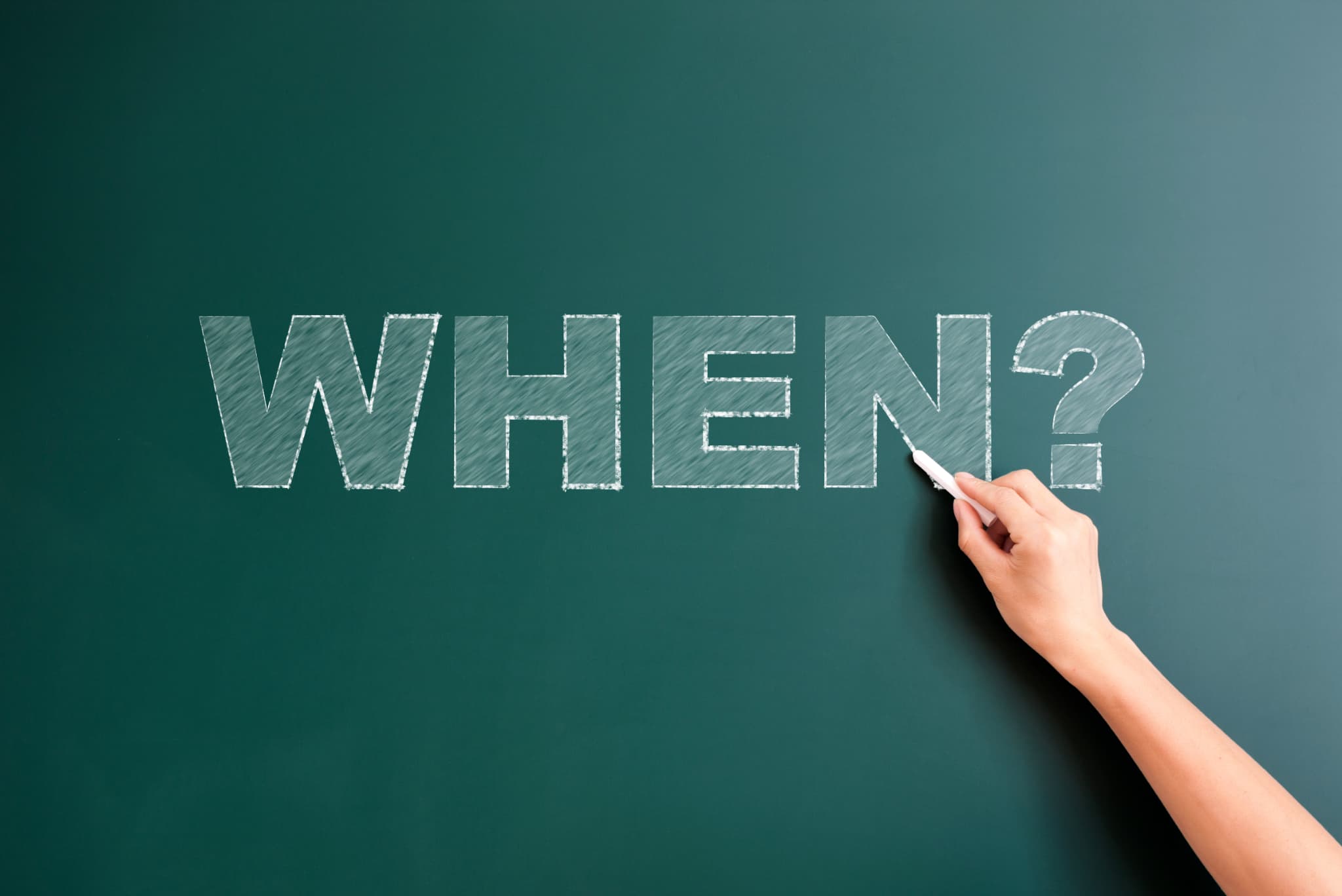 チョークで書かれた黒板のWHEN？の文字を示して矯正治療で抜歯をするタイミングを説明するイメージ
