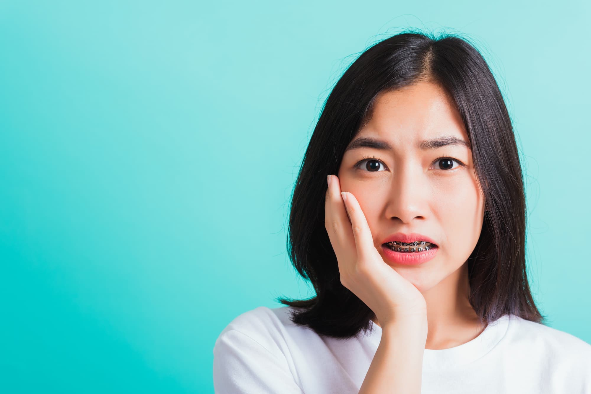 ワイヤー矯正中に口内炎ができて痛む頬をおさえる女性