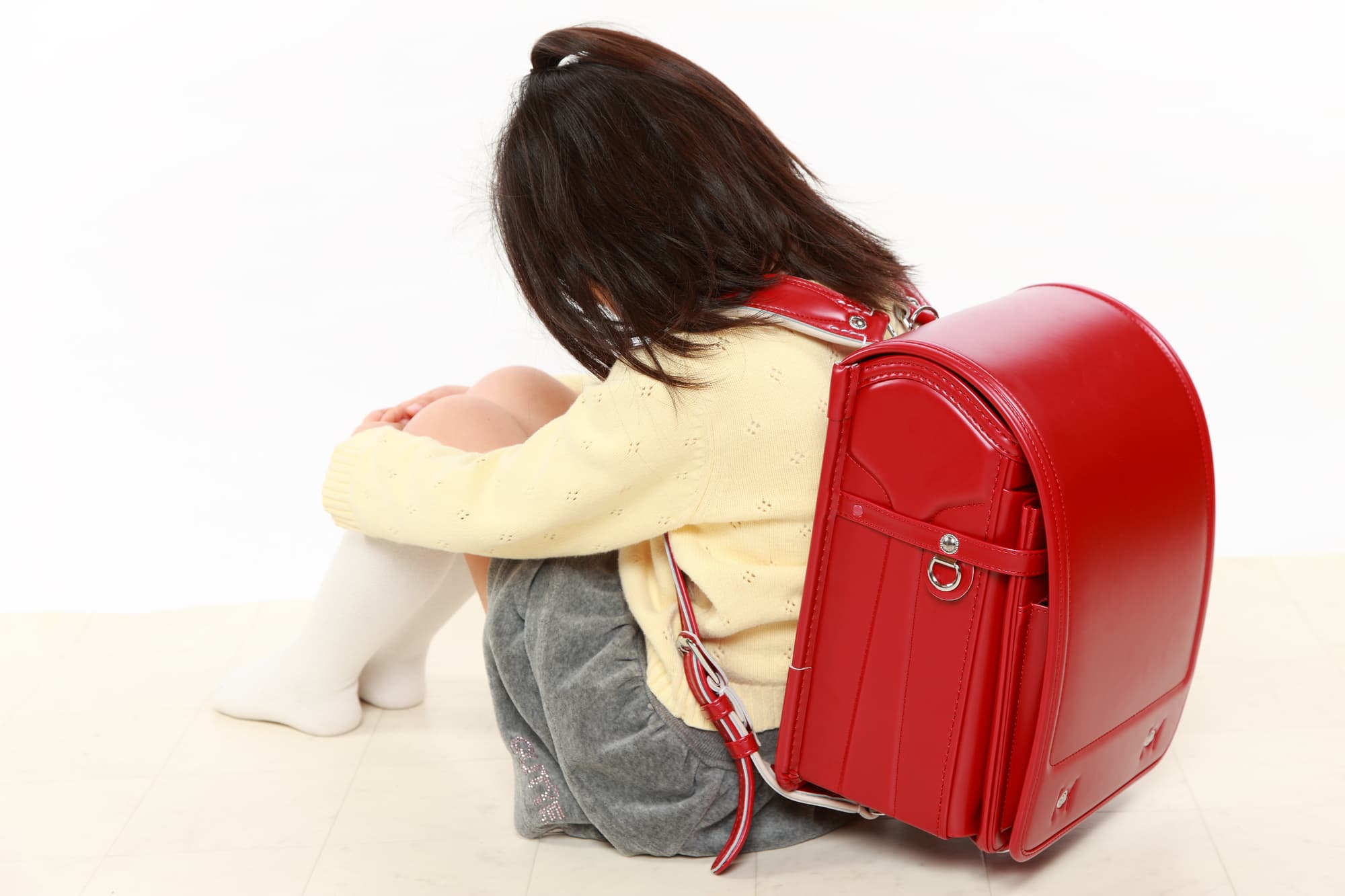 八重歯がコンプレックスでうつむいて膝を抱えて座る小学生